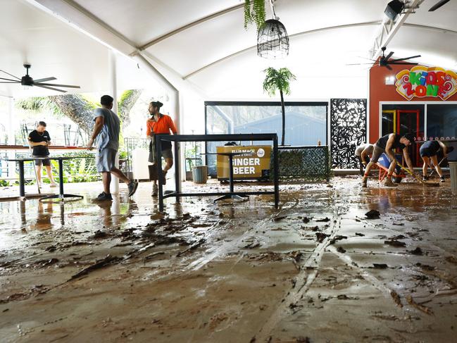 Ellis Beach Bar and Grill staff members scrape up thick mud from the floor after debris caused by flooding rain tore through the popular beachside eatery on Sunday. Picture: Brendan Radke