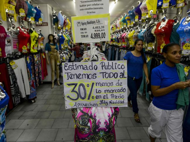 People watch the window of a store displaying signs informing of a 30% discount, in Caracas on December 9, 2016. The Venezuelan government ordered the owners of shops selling clothing, footwear and accessories to reduce their prices by 30% during Christmas. / AFP PHOTO / FEDERICO PARRA