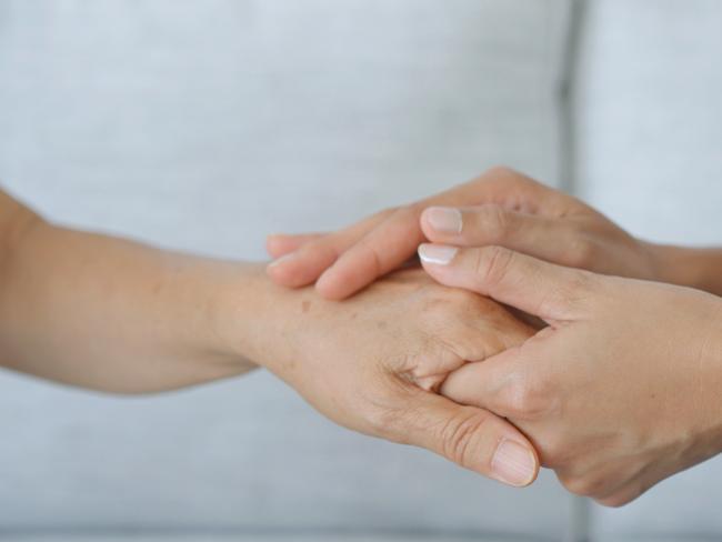 home caregiver holding hands and consoling Asian senior woman during a home visit