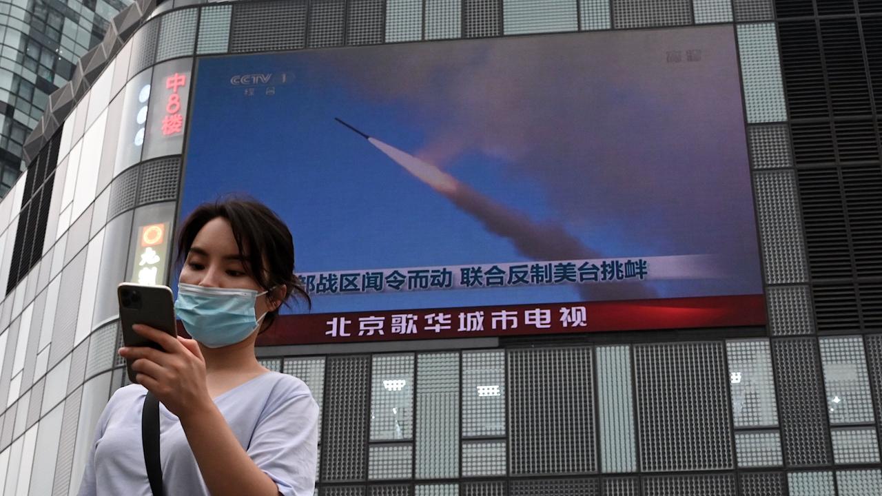 A woman in Beijing uses her mobile phone as she walks in front of a large screen showing a news broadcast about China's military exercises encircling Taiwan. (Photo by Noel Celis / AFP)