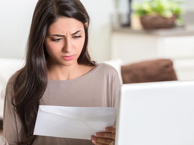 Distraught woman working on her bills at home. She is going through her mail and paper bills, she also has her laptop in front of her.