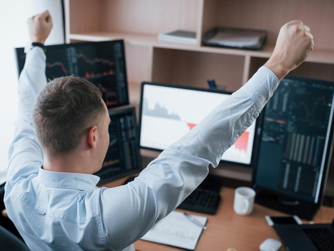 Hands up because of success. Man working online in the office with multiple computer screens in index charts.. happy investor generic