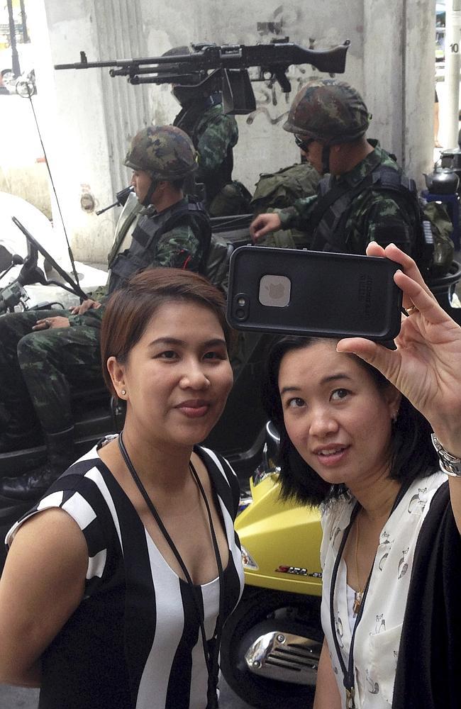 Passersby pose as Thai army soldiers sit in a jeep mounted with a machine gun. Picture: AFP