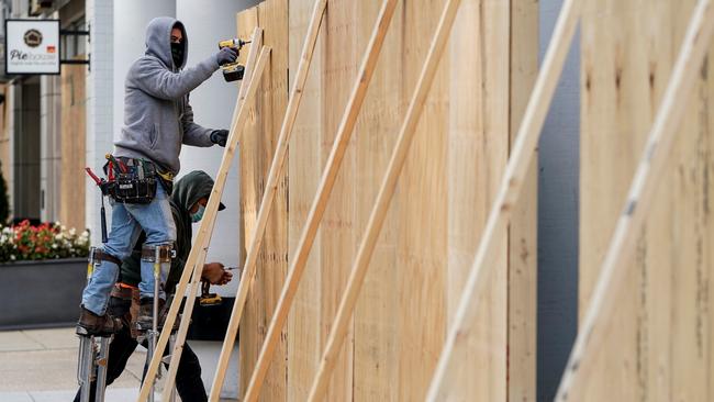 Workers cover shop fronts with plywood near the White House on Sunday. Picture: Reuters