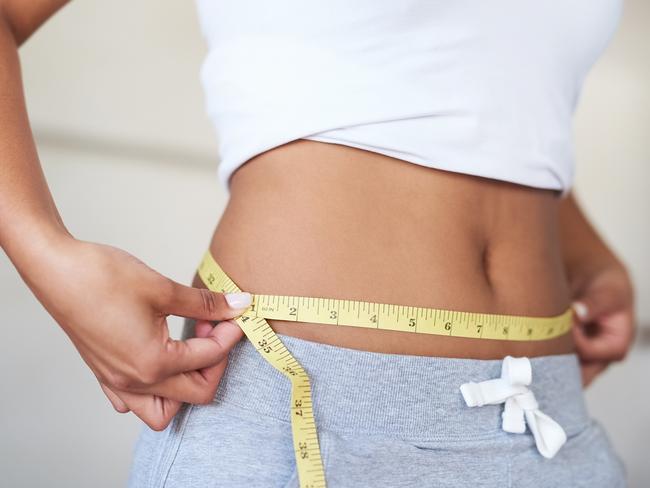 Cropped shot of a young woman measuring her waist in the bathroom