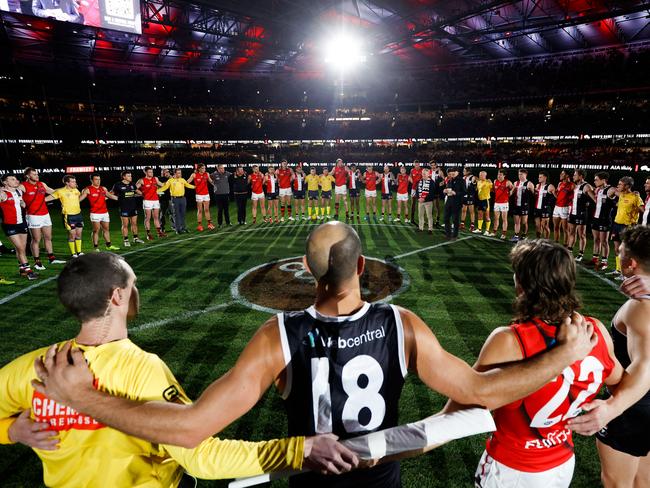 MELBOURNE, AUSTRALIA - JUNE 17: Players, coaches and umpires huddle as Tim Watson and Nathan Burke speak before Spuds Game during the 2022 AFL Round 14 match between the St Kilda Saints and the Essendon Bombers at Marvel Stadium on June 17, 2022 in Melbourne, Australia. (Photo by Michael Willson/AFL Photos via Getty Images)