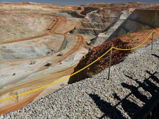 Visitors cast shadows as they look out over part of the main pit of Newcrest Mining Ltd.'s Telfer Mine in the Pilbara region of Western Australia Thursday, July 28, 2005. The mine, which was officially opened today, will be Australia's largest gold and copper producer. Photographer: Will Burgess/Bloomberg News