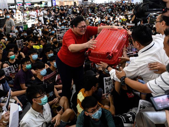 TOPSHOT - A tourist (C) gives her luggage to security guards as she tries to enter the departures gate during another demonstration by pro-democracy protesters at Hong Kong's international airport on August 13, 2019. - Protesters blocked passengers at departure halls of Hong Kong airport on August 13, a day after a sit-in forced authorities to cancel all flights to and from the major international hub. (Photo by Philip FONG / AFP)