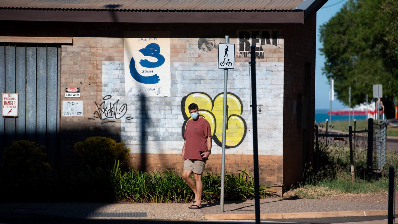 A man walks past a poster from artist Peter Drew entitled Together Soon Enough at Darwin’s Waterfront. Picture: Che Chorley