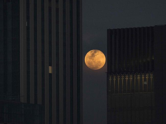 The moon rises between two office buildings in Bangkok. Picture: AFP/Lillian Suwanrumpha