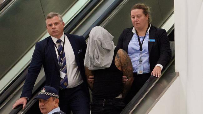 With a t-shirt over his head to hide his face, the young man was led out of the terminal in handcuffs by NSW Police detectives attached to Strike Force Pemak on Sunday. Picture: NSW Police