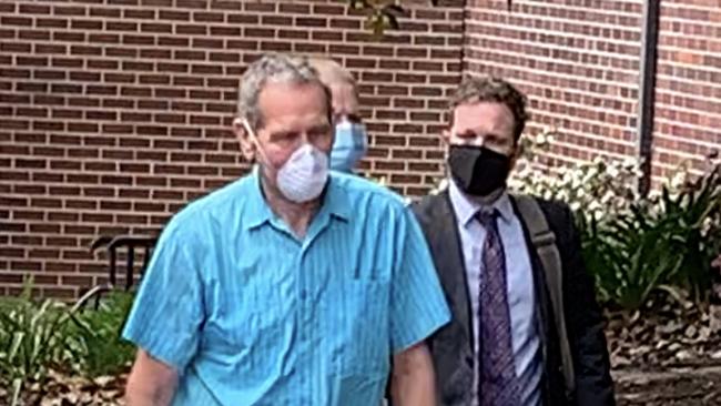 Brenton Lowe (middle, behind) wearing a blue mask and attempting to avoid getting his picture taken by walking behind two men. Picture: Madelaine Wong