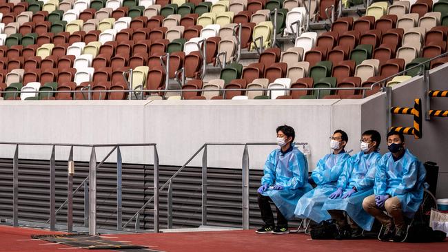 Staff members in protective clothing and masks next to empty seats during a test event in Tokyo. Picture: AFP