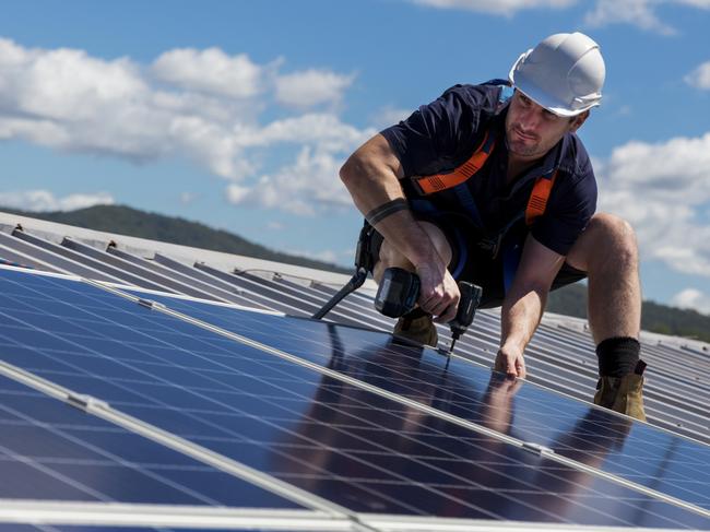 TRADESMAN/ TRADIE/BUILDING INDUSTRY:  Solar panel installer with drill installing solar panels on roof on a sunny day