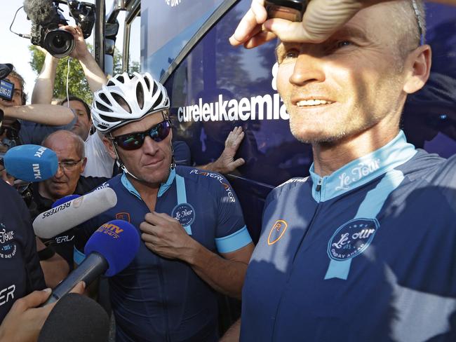 Lance Armstrong looks on as former England footballer Geoff Thomas speaks to journalists.