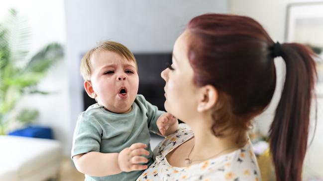 A mother holding child baby on the living room. The baby is sick having some cough. Istock Photo