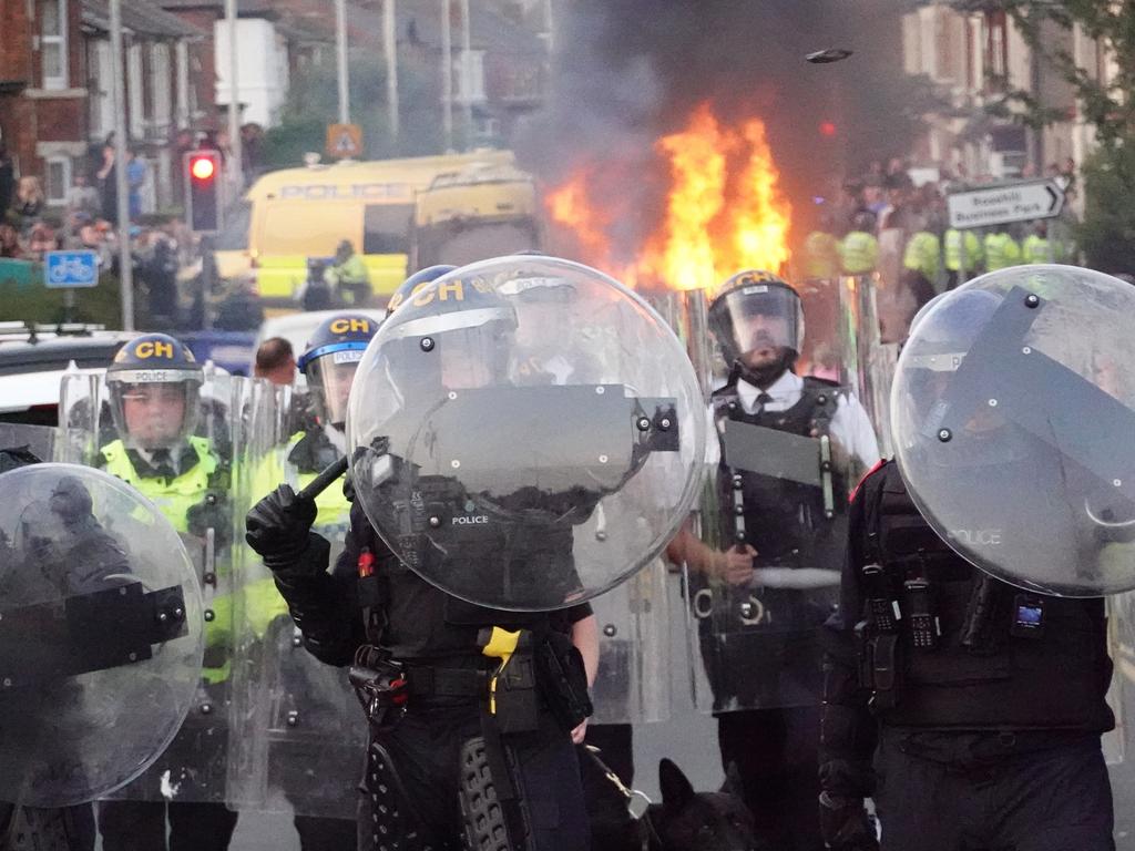 A policeman deflects a brick thrown by protesters near a burning police vehicle in Southport, England. Picture: Getty Images