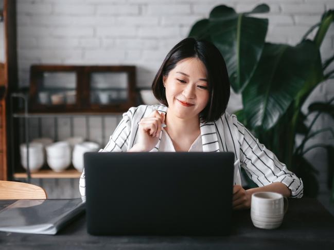 Young Asian woman having online business meeting, video conferencing on laptop with her business partners, working from home in the living room