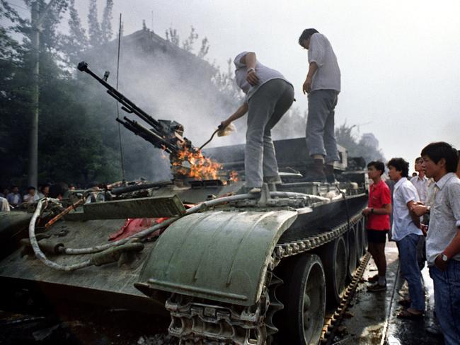 People check a burning armoured personnel carrier which was set on fire by rioters during clashes with army forces near Tiananmen Square in Beijing in 1989. Picture: AFP