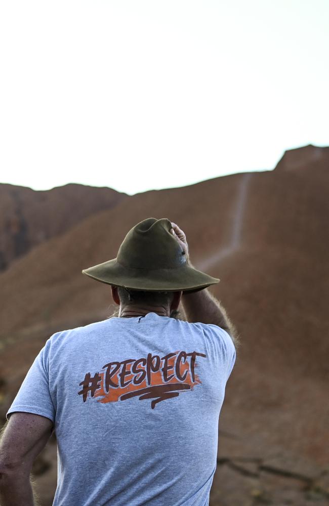 A man wearing a T-shirt saying 'I chose not to climb' stands next to tourists lining up to climb Uluru, also known as Ayers Rock at Uluru-Kata Tjuta National Park on Friday. Picture: AAP