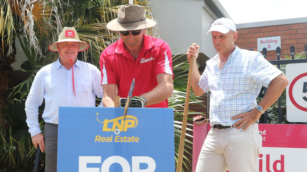 Member for Barron River, Craig Crawford slices through a “For Sale” sign as Member for Cairns, Michael Healy and ALP candidate for Mulgrave, Richie Bates look on.