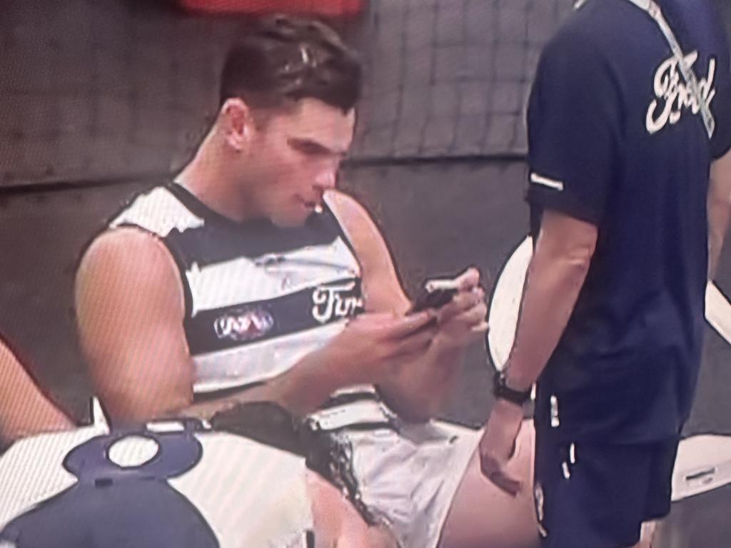 Tom Hawkins looking at a Cats’ official’s phone during the lightning delay.