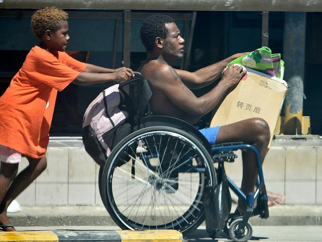 A boy pushes the wheelchair of a family member in downtown Honiara as they flee to higher ground. Picture: AFP.