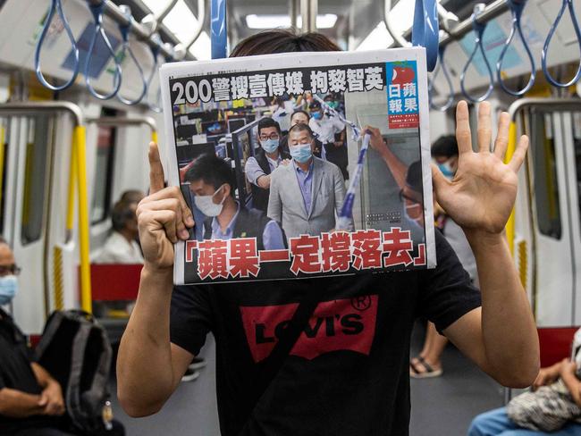 A commuter holds a copy of the Apple Daily newspaper while gesturing the pro-democracy slogan âfive demands, not one lessâ inside a train in Hong Kong on August 11, 2020, a day after authorities conducted a search of the newspaper's headquarters after the companyâs founder Jimmy Lai was arrested under the new national security law. - Hong Kong pro-democracy media tycoon Jimmy Lai was arrested on August 10 and led in handcuffs through his newspaper office as police raided the building, part of a sweeping crackdown on dissent since China imposed a security law on the city. (Photo by ISAAC LAWRENCE / AFP)