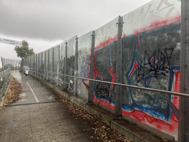 Graffiti on glass panels along a pedestrian walkway above the multi-lane roadway at the intersection of Warringah Rd and Forest Way at Frenchs Forest in March 14, 2023. Picture: Jim O'Rourke