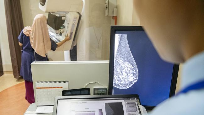 Female patient receiving breast scan, radiographer looking at medical image on screen