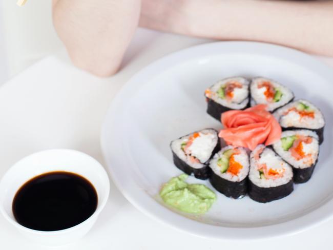 Young woman eating sushi at Japanese restaurant. Asian nutrition. Roll. Fast food delivery. Red fish, rice, soy sauce. Healthy