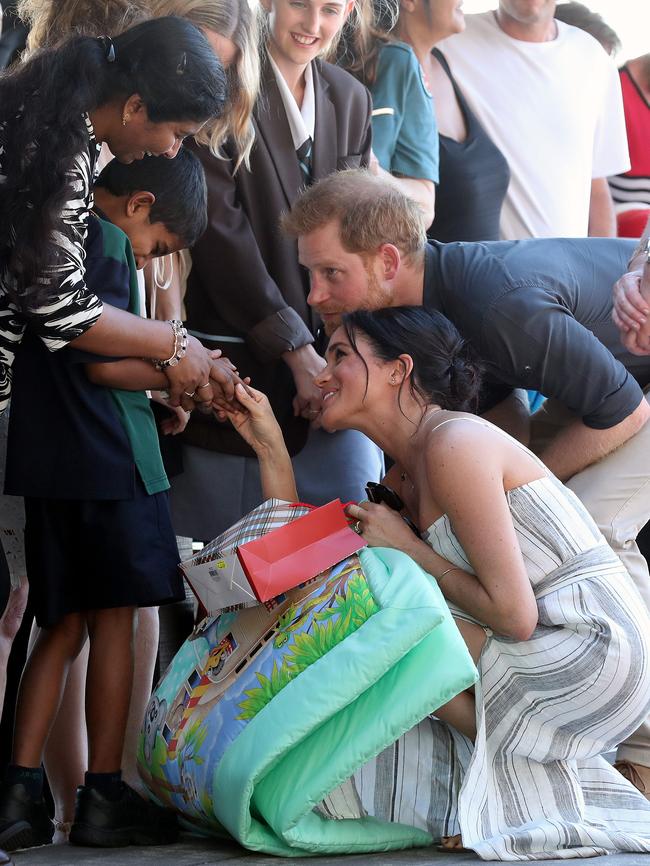 Harry and Meghan crouch down to touch hands with a young boy during their walk along Kingfisher Bay pier. Picture: Liam Kidston