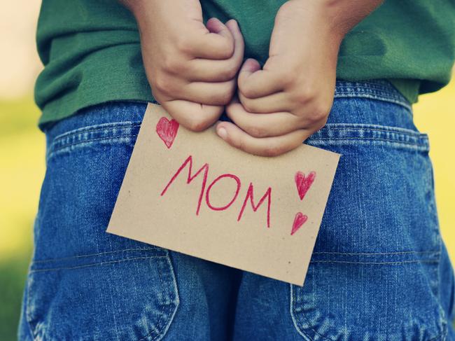 Young child with a nice note for his mother behind his back.