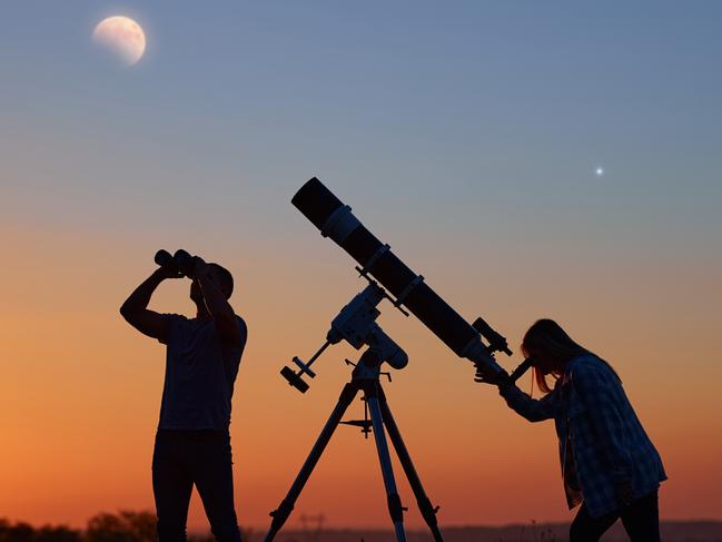 Couple stargazing together with a astronomical telescope, looking at planets, stars, lunar eclipse and meteor shower.