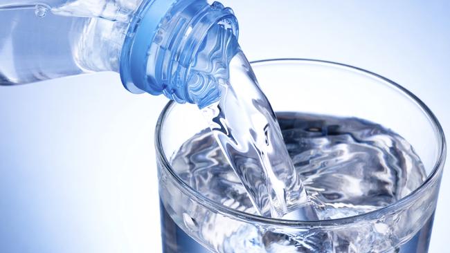 Close-up Pouring glass of water from a plastic bottle on blue background