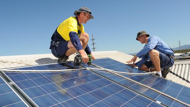 Solar Power, Electrician Adam Garrett (blue) and Robbie Mead (yellow)working on roof top solar panels.