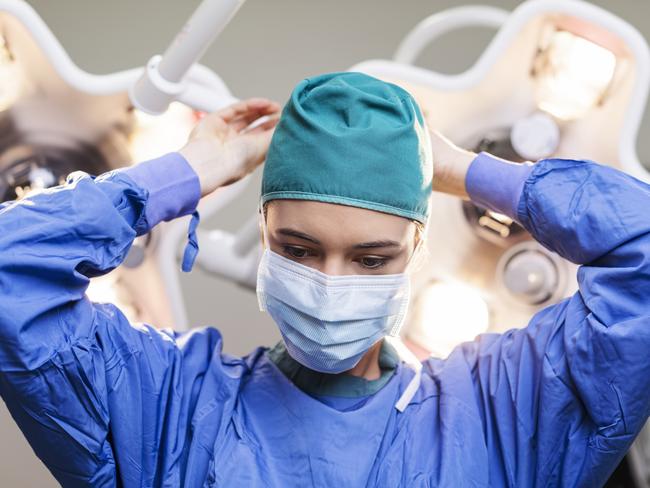 Female surgeon wearing surgical mask. Skilled doctor is working in operating room. She is in hospital.