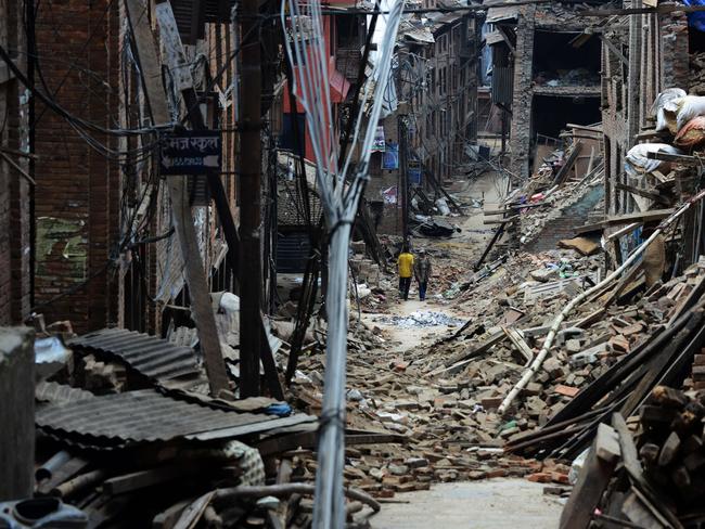 Nepalese residents walks past damaged houses following an earthquake in Bhaktapur on the outskirts of Kathmandu on May 13, 2015. Rescuers were battling to reach survivors of a deadly new earthquake in Nepal that triggered landslides and brought down buildings, as the search continued for a US military helicopter that went missing while delivering aid. Thousands of traumatised survivors spent the night outdoors, afraid to return to their houses after the 7.3-magnitude quake hitMay 12, 2015, less than three weeks after the country was devastated April 25, 2015 by its deadliest quake in more than 80 years. AFP PHOTO / PRAKASH MATHEMA