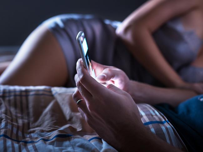 Man using smartphone and ignoring sexy woman in bed at night. Looking at mobile phone. Husband giving no attention to wife. Disregarding marriage. Couple problem. Cellphone addiction. Obsessed addict.