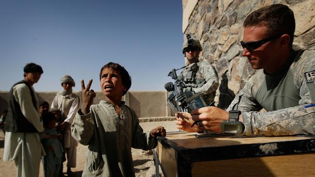 An Afghan boy ask a translator for more money as Capt. Nicholas Stout of Lake Orion, Michigan (R) holds the pay for participating in a jobs program sponsored by the 101st Airborne Division of the US Army in 2010.