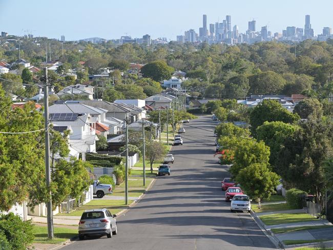 Developing Queensland - Brisbane - Residential houses street against Brisbane City skyline.