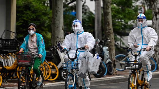 Workers wearing PPE cycle on a street during a Covid lockdown in Shanghai. Picture: Hector Retamal/AFP