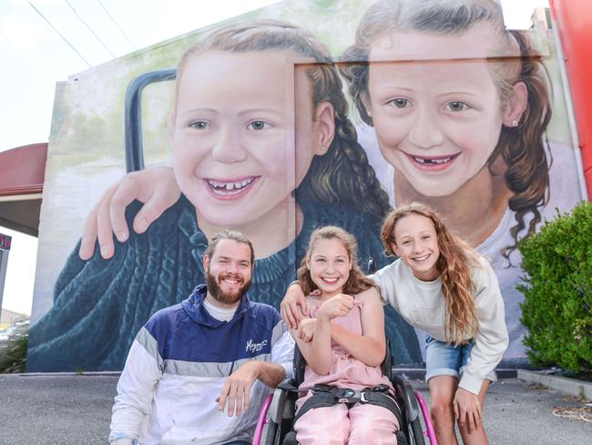 DECEMBER 4, 2021: Artist Sam Brooks in front of the 8-meter-tall mural he painted of Variety grant recipient, Chloe, centre, and her sister Lily. Picture: Brenton Edwards