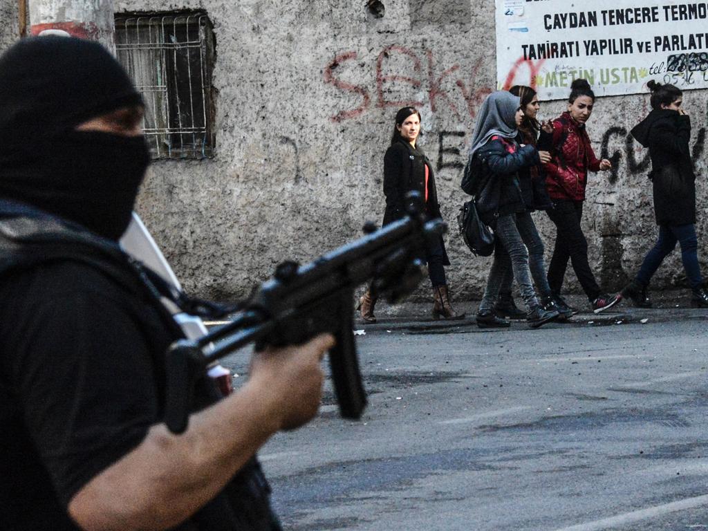 People walk by a Turkish police officer holding an assault riffle during clashes with protestors demonstrating against government imposed curfews imposed on areas of eastern Turkey, on February 15, 2016 in Diyarbakir. Picture: AFP / ILYAS AKENGIN