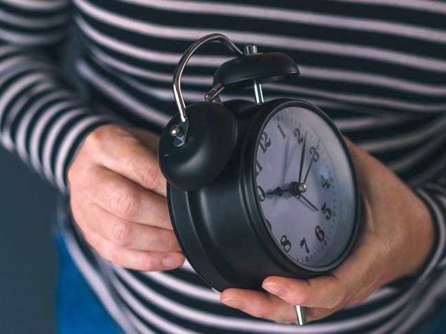 Woman winding retro alarm clock, concept of daylight saving time, selective focus