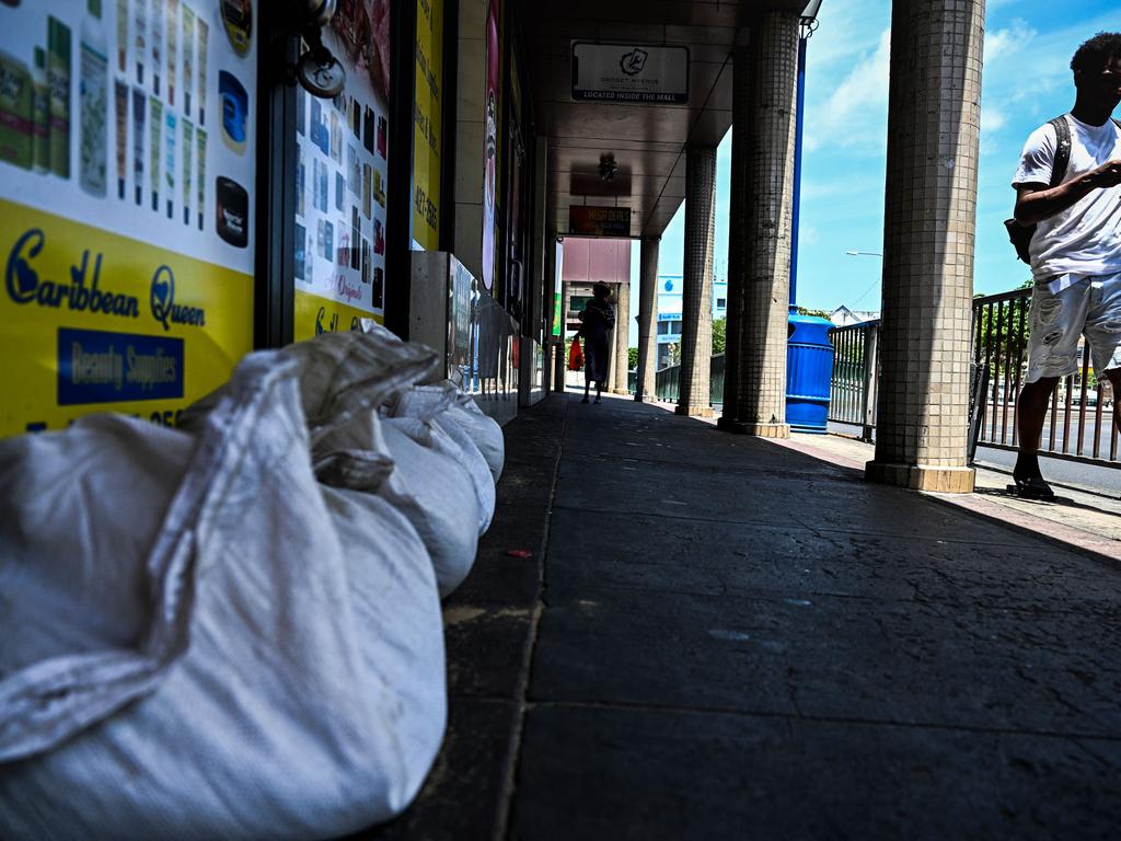 A man walks past bags of sand outside of a shop in Bridgetown, Barbados. (Photo by CHANDAN KHANNA / AFP)