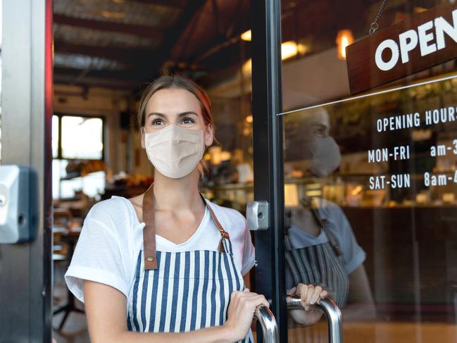Happy business owner opening the door at a cafe wearing a facemask to avoid the spread of coronavirus ÃÂ¢Ãâ¬Ãâ reopening after COVID-19 concepts