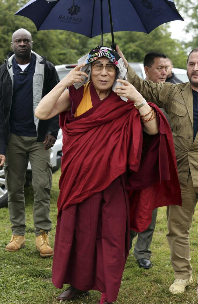 Spiritual leader Dalai Lama wears a Glastonbury Festival T-shirt on his head as he arrives in the rain, at Worthy Farm in Somerset. Picture: AAP