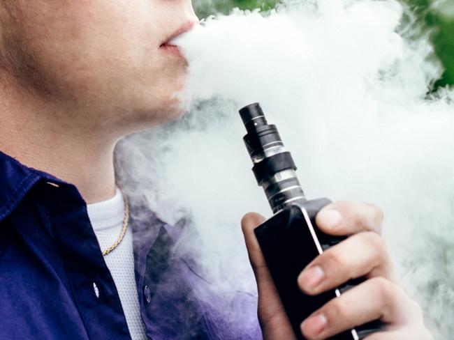 A young adult male has a cloud of nicotine vapor "smoke" pouring from his mouth.  Vape smoking, or "vaping" is growing in popularity, as well as falling under stricter state and governmental regulations.  Horizontal image with copy space.