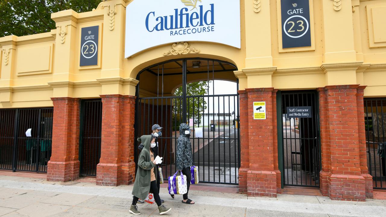 People wearing masks and carrying toilet paper walk past Caulfield Racecourse in Melbourne on Saturday. Picture: Vince Caligiuri/AAP